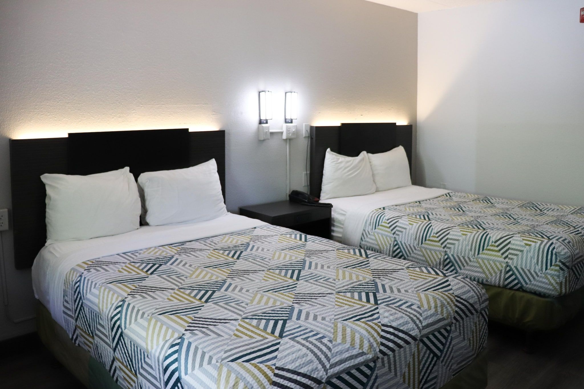 Une chambre d’hôtel avec deux lits, chacun recouvert d’une couvre-lit à motifs et agrémenté d’oreillers blancs. Une table de chevet avec une lampe se trouve entre les deux lits.