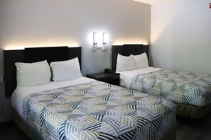 Habitación de hotel con dos camas, cada una con una colcha estampada y almohadas blancas. Hay una mesita de noche con una lámpara entre las camas.