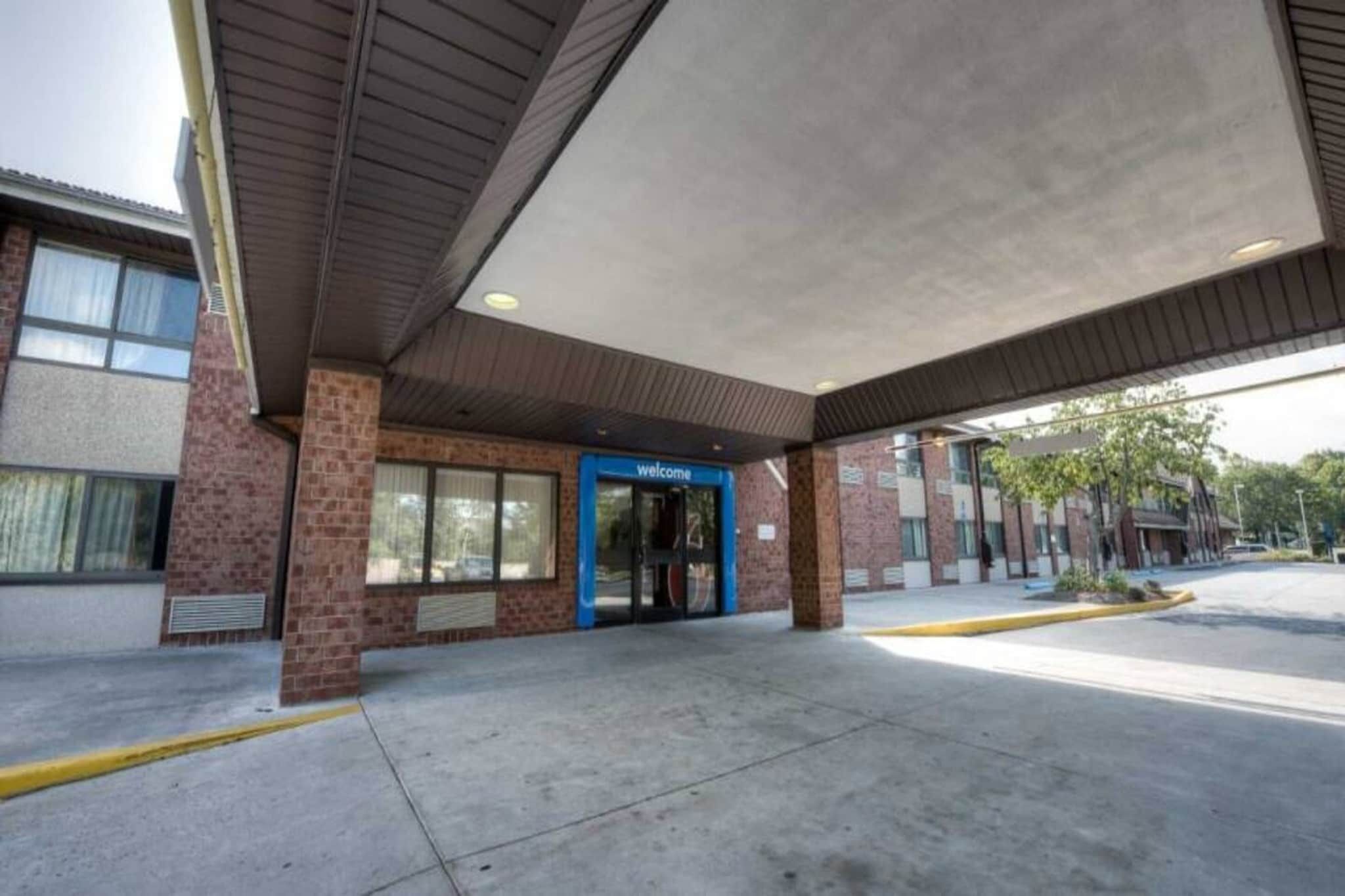 A building with a blue entrance marked 'welcome,' a brick facade, and a covered parking area.