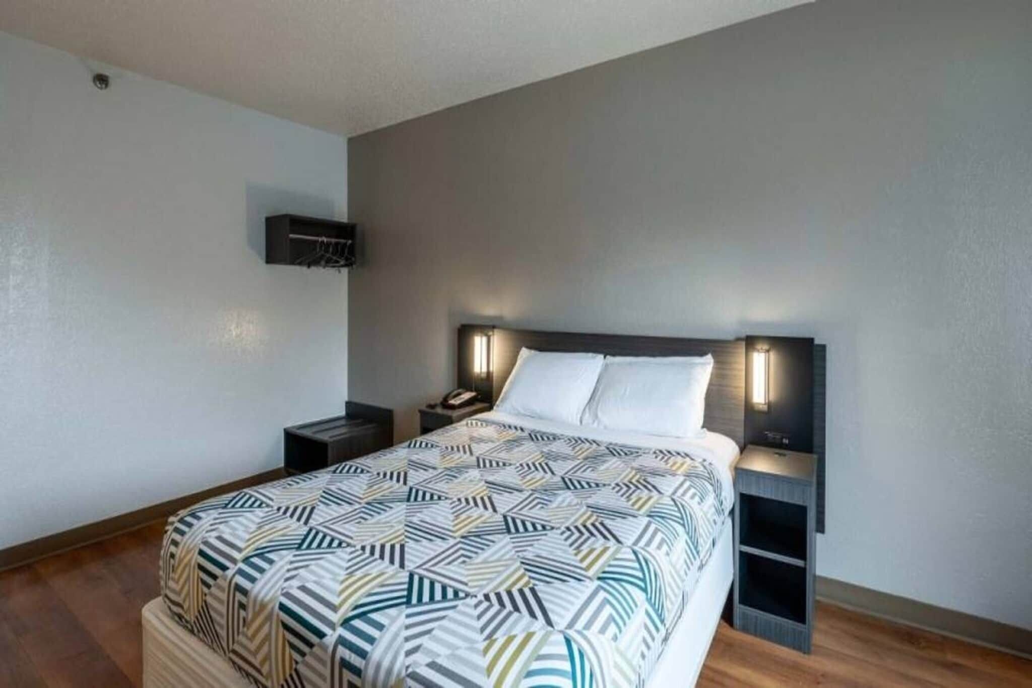 A hotel room with a bed, bedside tables, a wall-mounted TV, and a patterned bedspread.