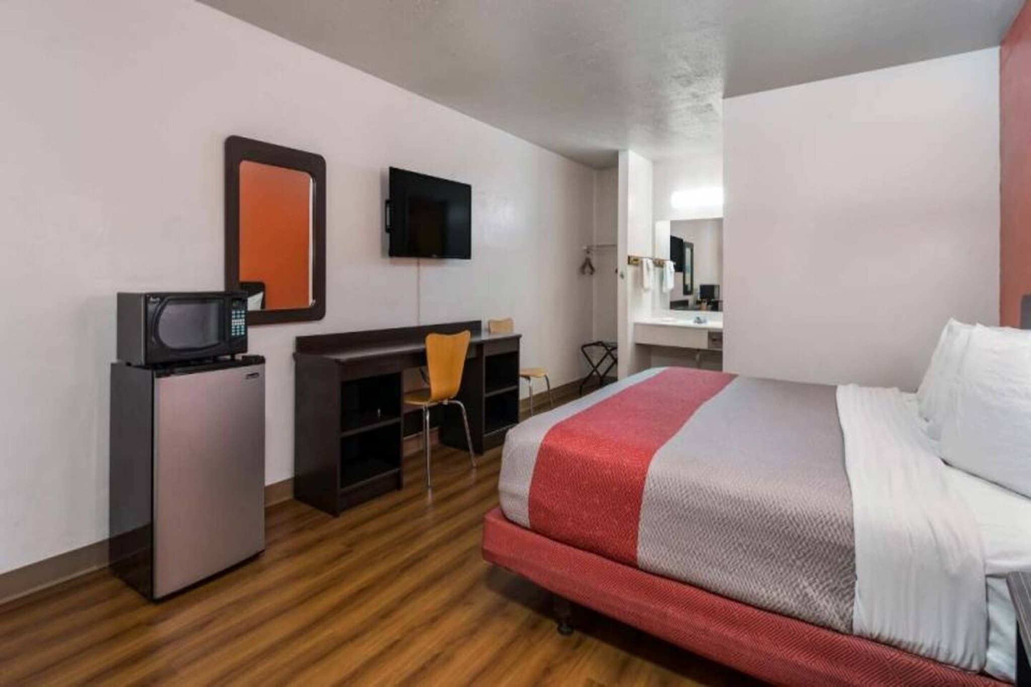 A hotel room with a bed, a desk, a chair, a television, and a small refrigerator.