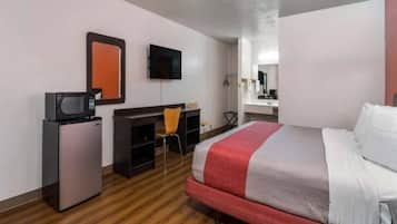 A hotel room with a bed, a desk, a chair, a television, and a small refrigerator.