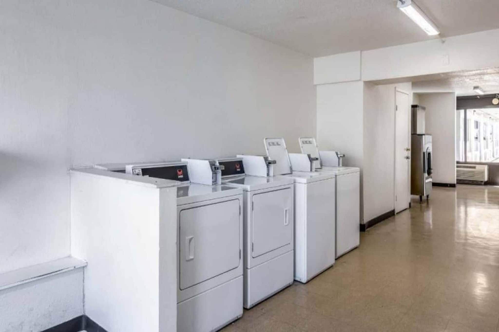 Een wasserette met meerdere wasmachines en drogers, een schone vloer en een eenvoudige muur.