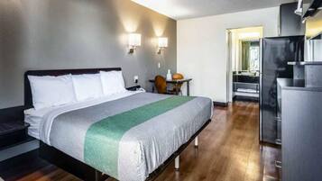Ein Hotelzimmer mit Bett, Schreibtisch, Stuhl, Kühlschrank und einem durch eine geöffnete Tür einsehbaren Badezimmer.