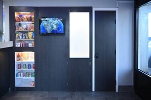 A room with a vending machine stocked with snacks and drinks, a television mounted on the wall, and a door. - 2 Queen Beds|NS| Kitchen (Little Rock AR)
