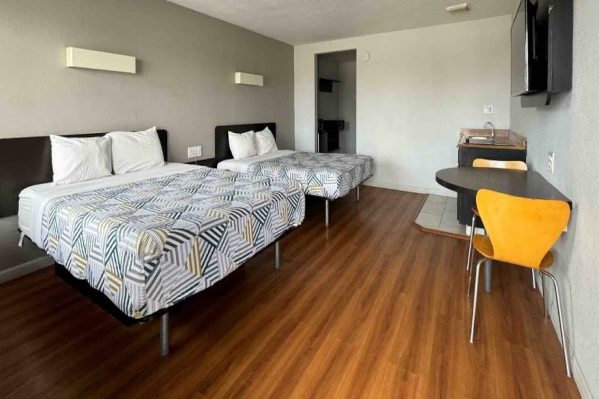 Une chambre d’hôtel avec deux lits, une petite table, une chaise et un téléviseur fixé au mur.