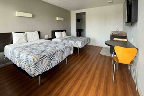 Een hotelkamer met twee bedden, een kleine tafel, een stoel en een aan de muur bevestigde televisie.