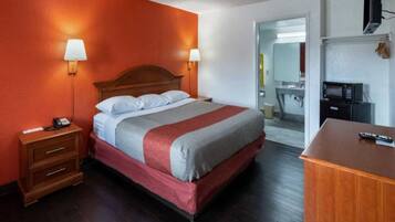 A hotel room with a bed, bedside tables, a desk, and a microwave.