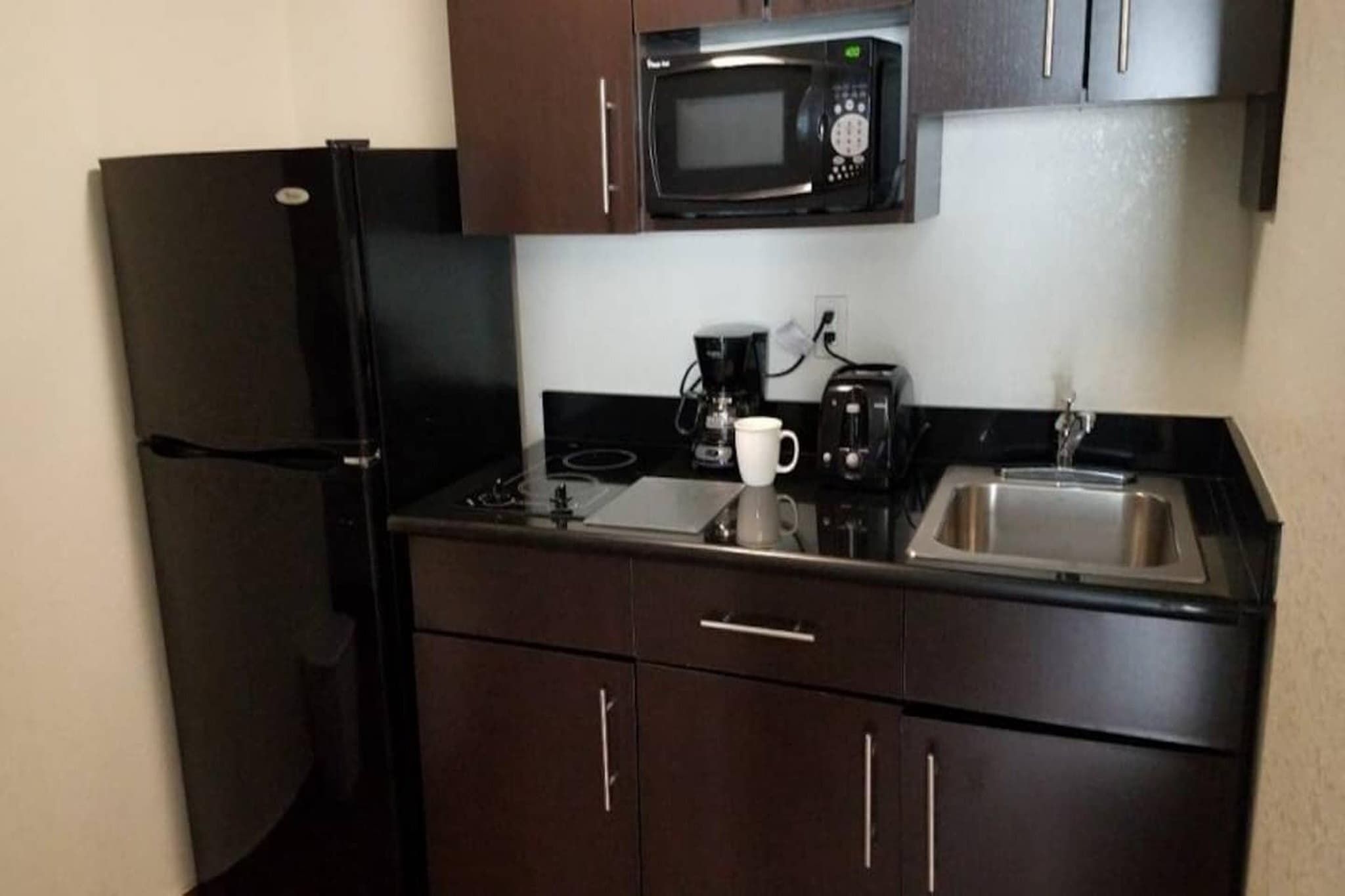 A compact kitchen with a refrigerator, microwave, coffee maker, and a coffee cup on the counter.