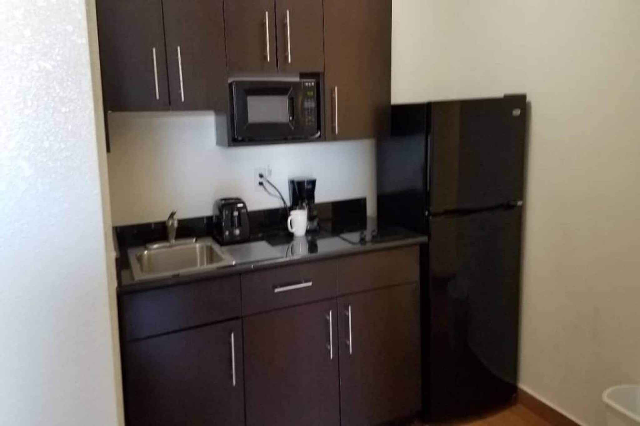 Una cocina compacta con armarios oscuros, un microondas, una cafetera y un refrigerador.