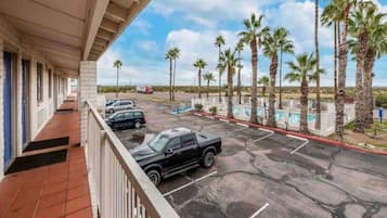 A parking area with a building in the background, a pool, and palm trees.