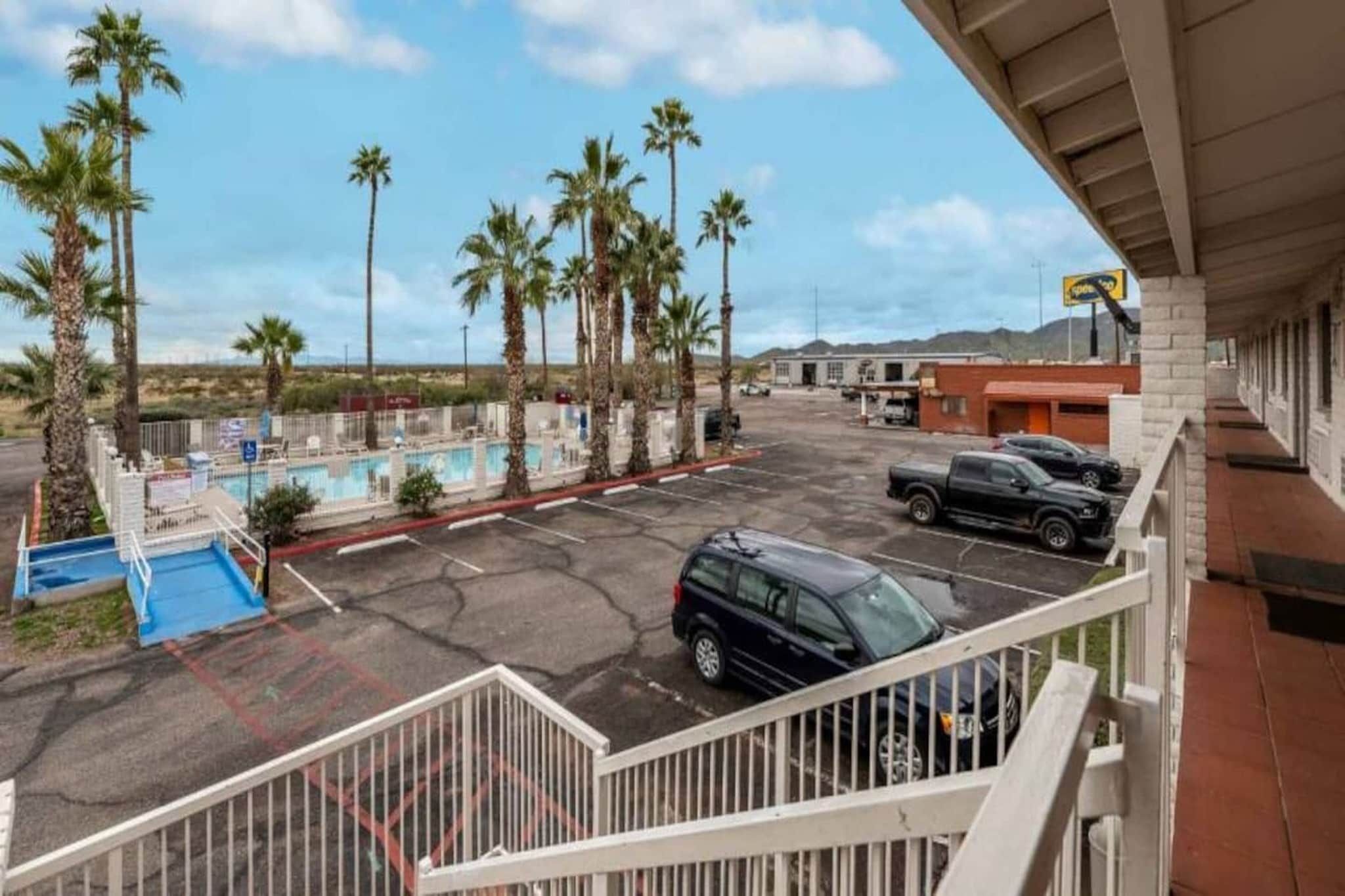A parking area with a pool, palm trees, and a building in the background.