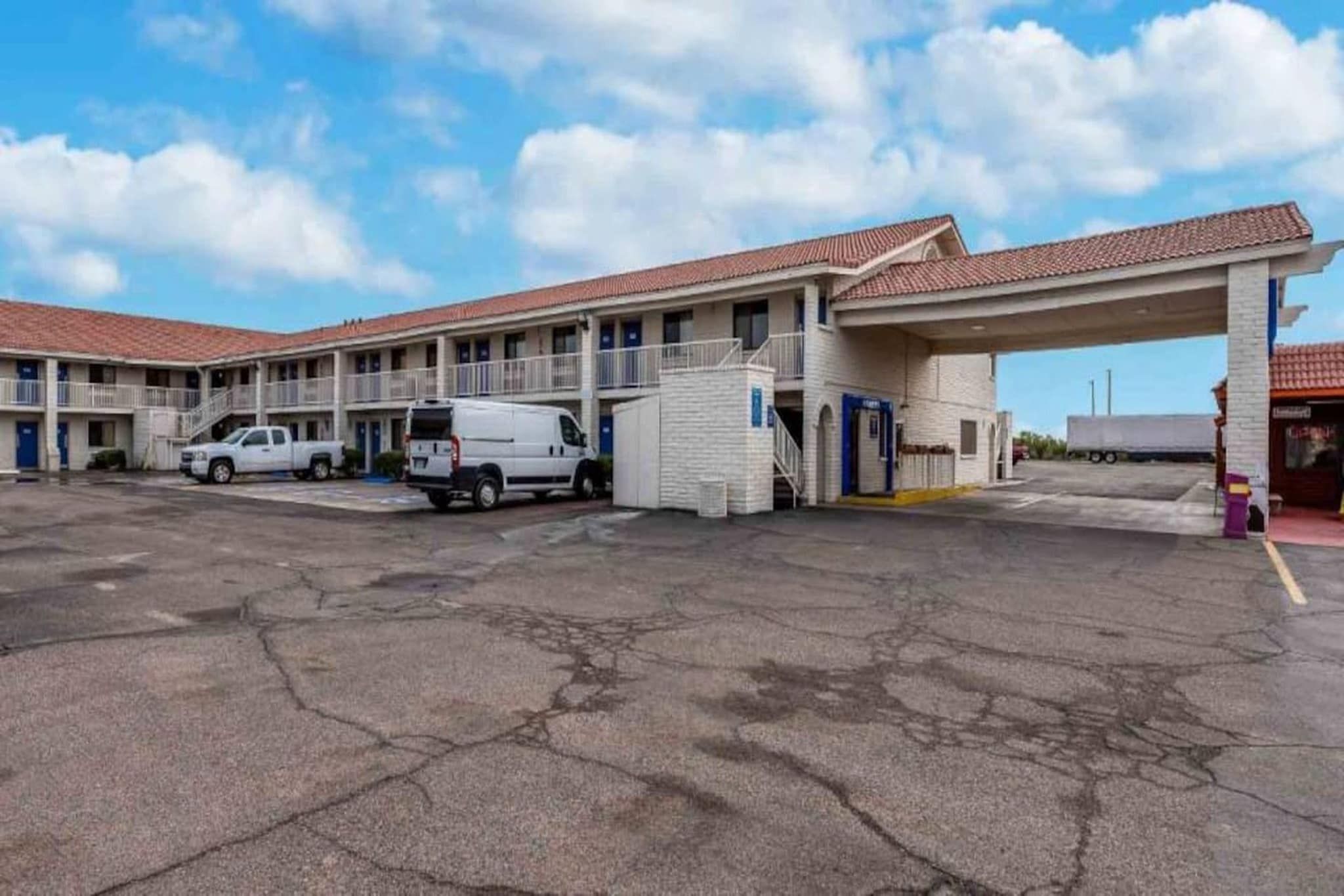 Un motel con estacionamiento, entrada cubierta y un edificio con techo de tejas rojas.