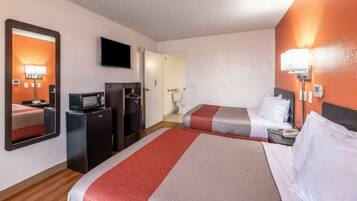 A hotel room with a large bed, a smaller bed, a desk with a computer, a TV, and a bathroom visible through an open door.