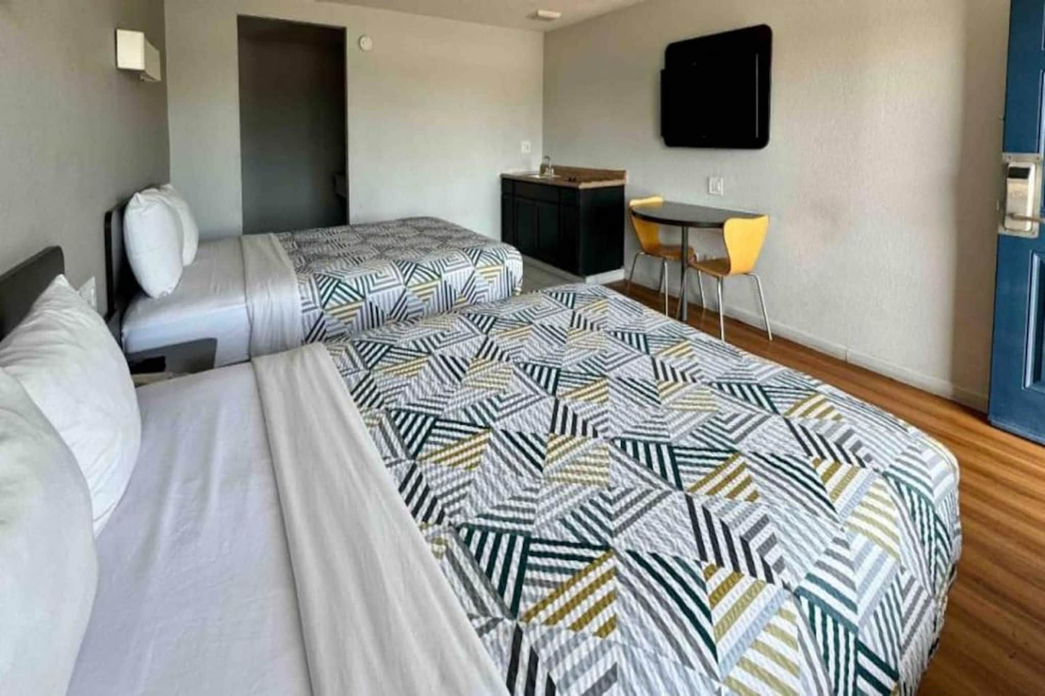 A hotel room with two beds, a desk, a chair, and a TV on the wall.