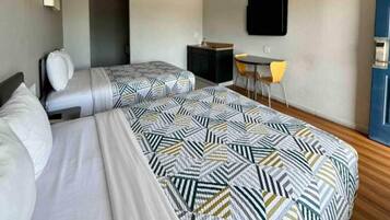 A hotel room with two beds, a desk, a chair, and a TV on the wall.