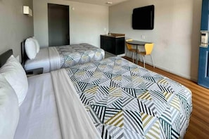 Een hotelkamer met twee bedden, een bureau, een stoel en een televisie aan de muur.