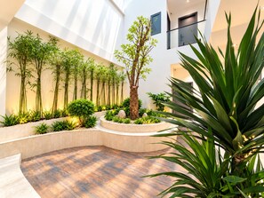 Un interior moderno con suelo de madera curva, un árbol central y plantas de bambú a lo largo de las paredes.