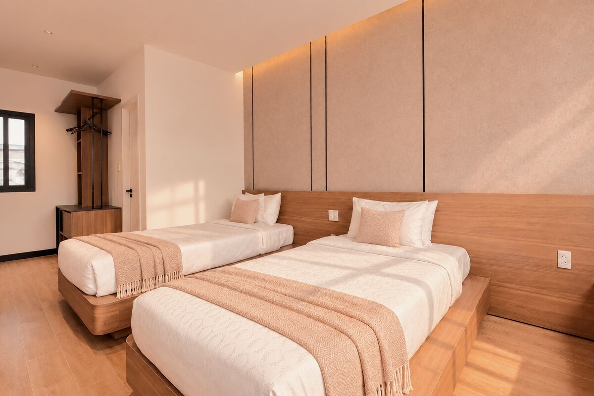 Una habitación de hotel moderna con dos camas, cabecero de madera, armario empotrado y un ventanal grande.