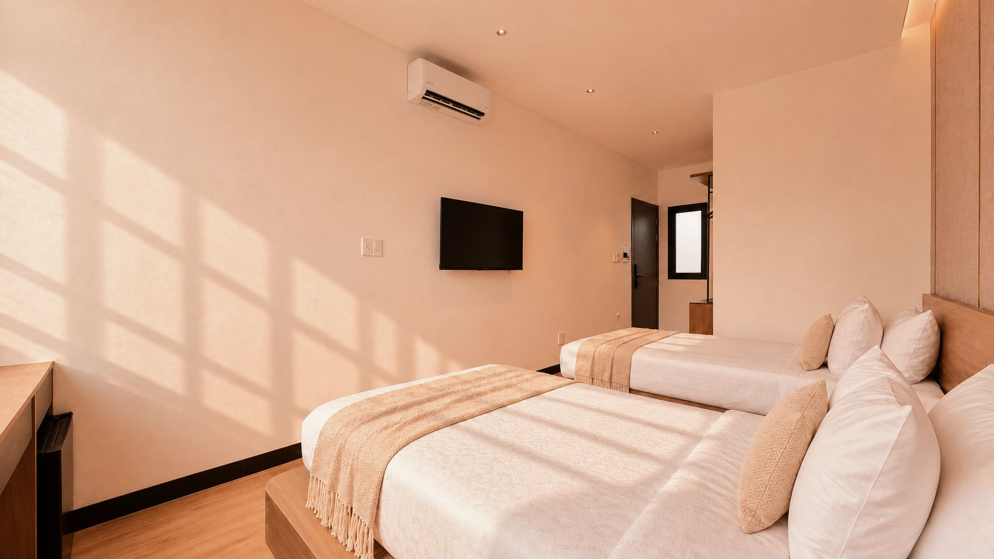 A modern hotel room with two beds, a flat-screen TV, and an air conditioning unit.