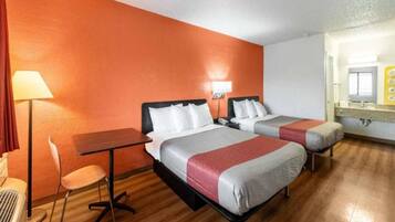 A hotel room with two beds, a desk, a chair, and a lamp.