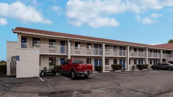 A multi-story motel with a parking lot, a red pickup truck, and a clear blue sky.