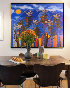 Ein Esstisch mit Stühlen, eine Blumenvase, eine Auswahl an Croissants, eine Tasse und ein Teekessel.