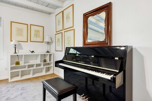 Ein Raum mit einem Klavier, einer Bank, einem Spiegel und gerahmten Kunstwerken an der Wand.