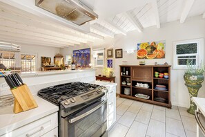 Eine moderne Küche mit Gasherd, Backofen und weißen Schränken. Auf der Arbeitsfläche befinden sich verschiedene Küchenutensilien und eine Weinflasche.