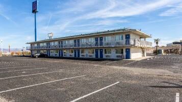 Ein Motel mit einer Reihe von Zimmern, einem Parkplatz und wolkenlosem Himmel.
