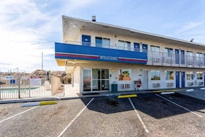 Un motel con un cartel de 'WELCOME', un estacionamiento y un área de piscina cercada.