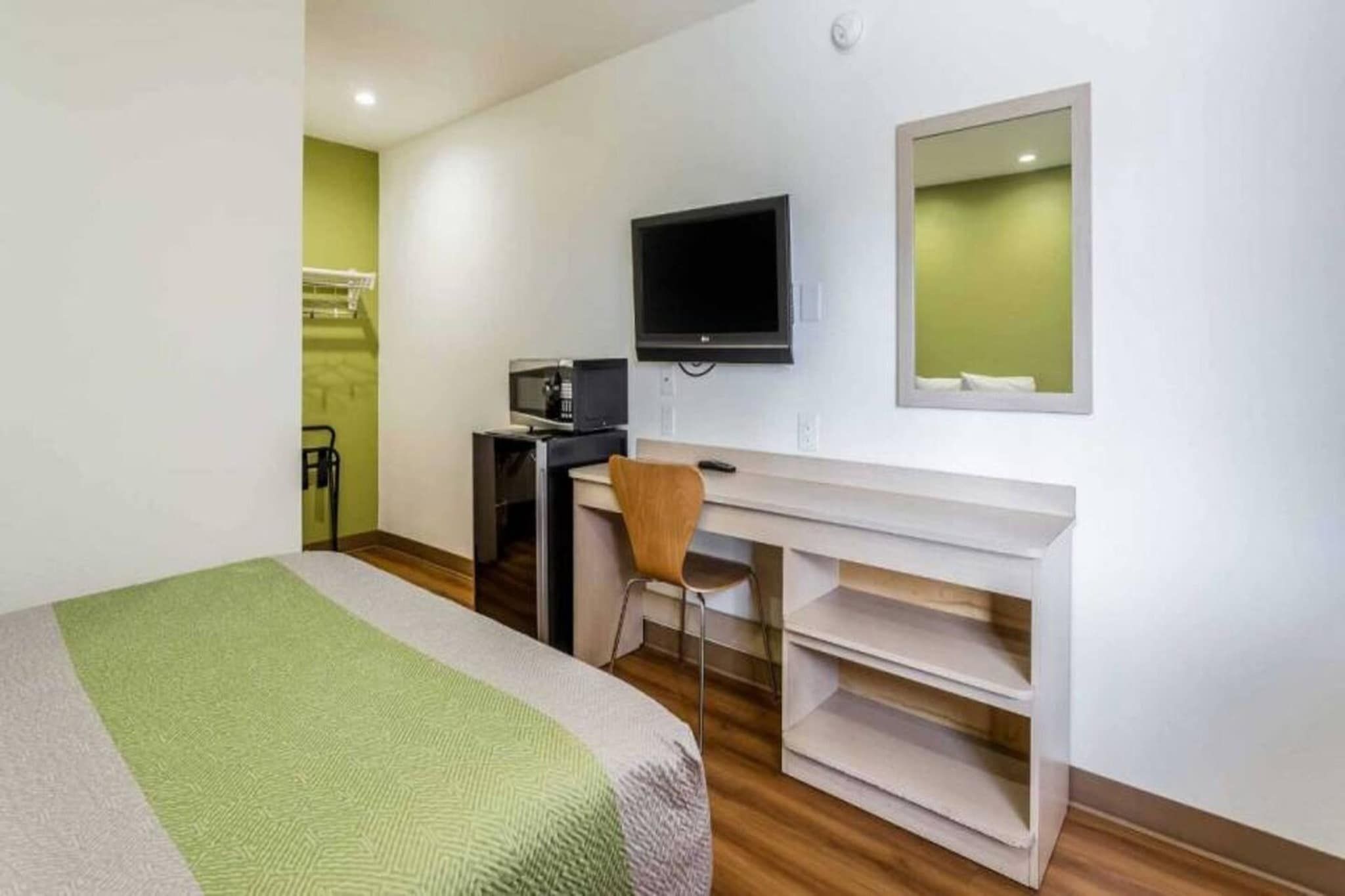 A hotel room with a bed, a desk with a chair, a television, and a small kitchenette.
