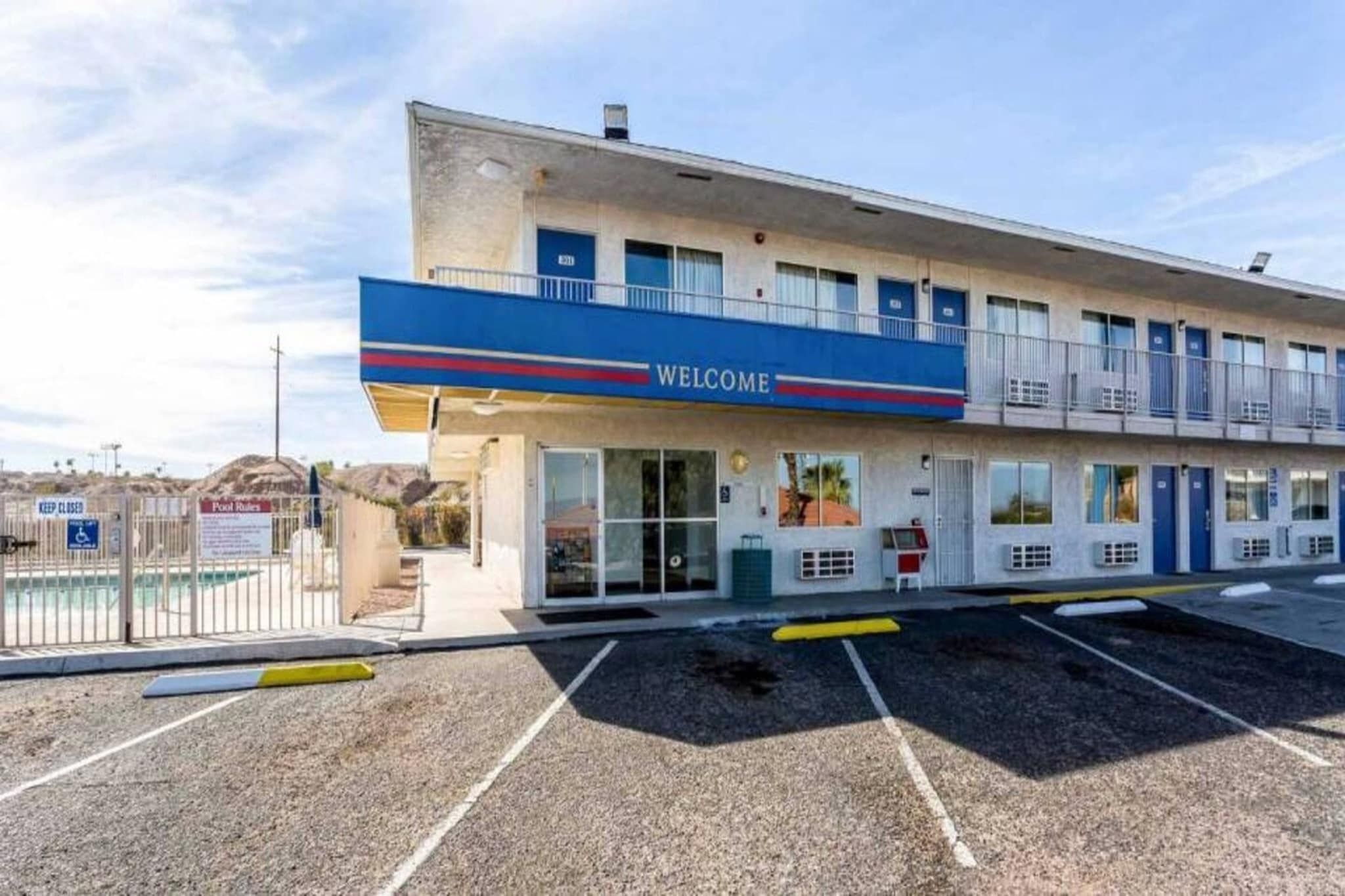 A motel with a 'WELCOME' sign, a parking lot, and a fenced pool area.