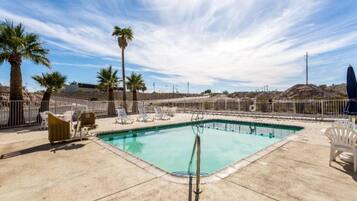 A swimming pool with lounge chairs and palm trees, surrounded by a fence.