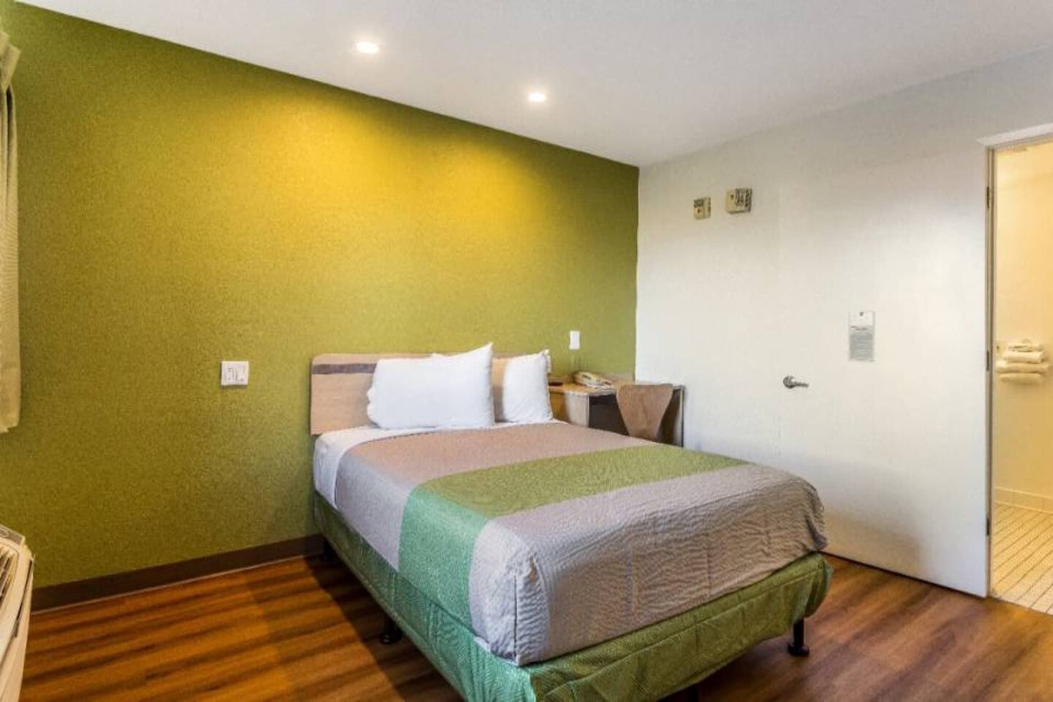 A single bed in a room with green walls, a wooden floor, and a white door.