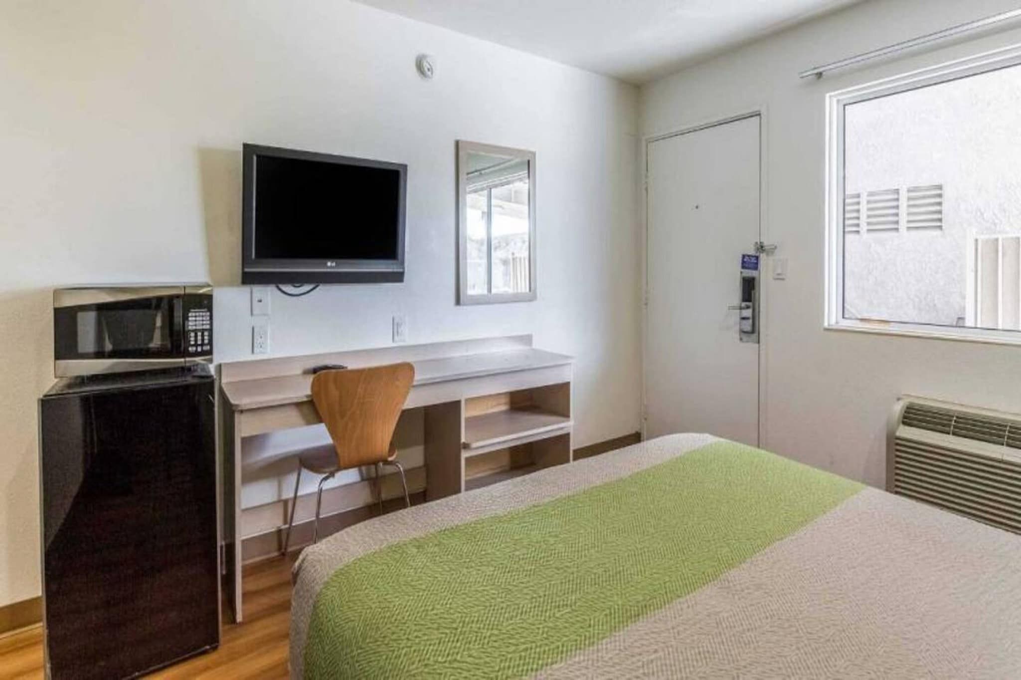Une chambre d’hôtel comprenant un lit, un bureau avec une chaise, une télévision, une fenêtre et une porte.