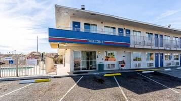A motel with a 'WELCOME' sign, a parking lot, and a fenced pool area.