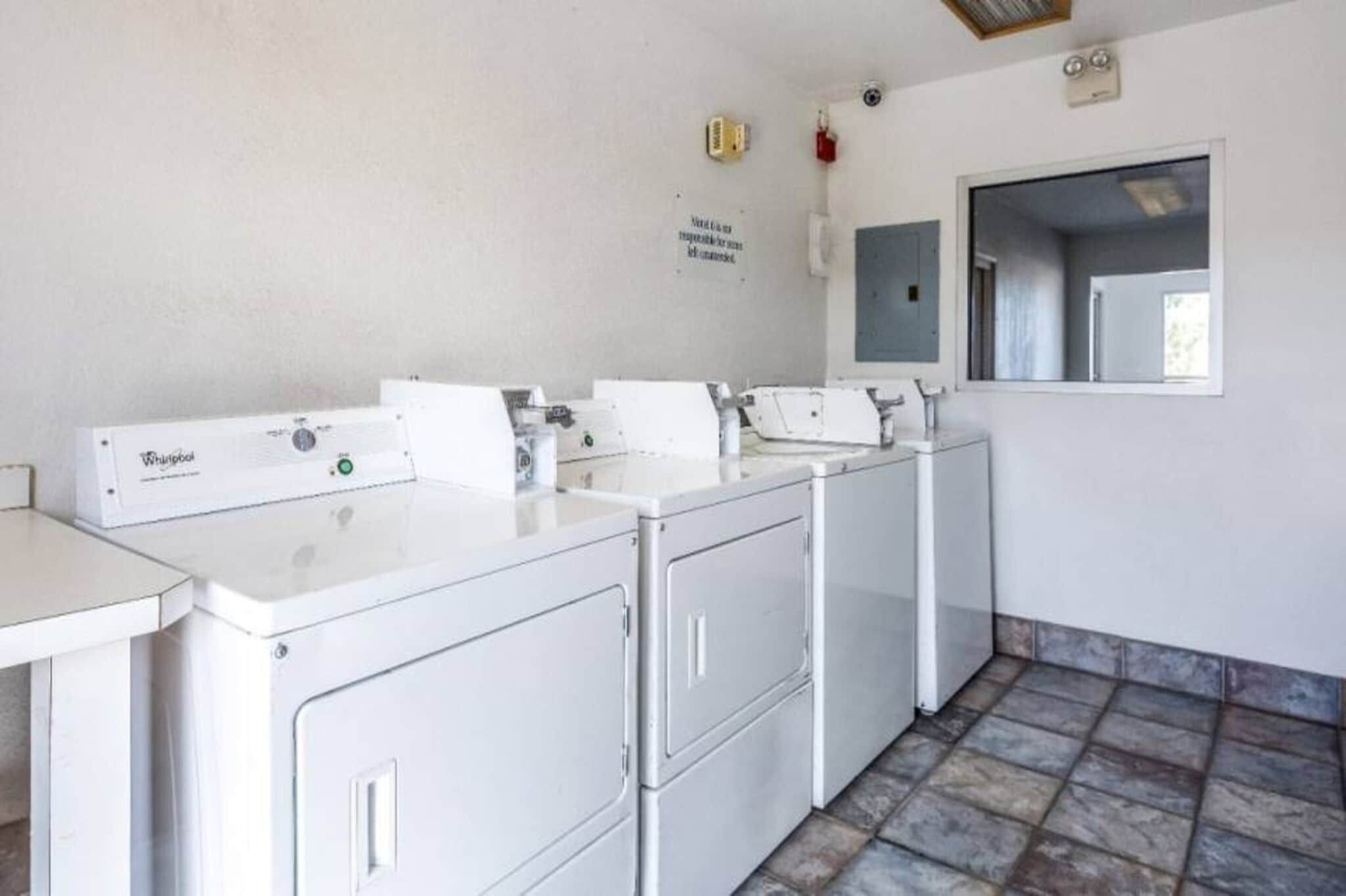 A laundry room with four Whirlpool washers and dryers, a white tiled floor, and a window with a view.