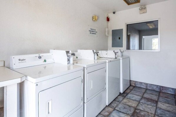 A laundry room with multiple Whirlpool washers and dryers, a tiled floor, and a window with a view. - 2 FULL BEDS | SMOKING (Needles)