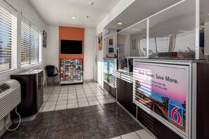 A hotel lobby with a reception desk, a magazine rack, and a large digital screen displaying a promotional message. - 1 Queen Bed | Non-Smoking (Temecula)