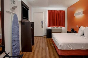 A hotel room with a bed, a TV, a desk, a chair, a red curtain, and a heater. - 1 Queen Bed | Non-Smoking (Temecula)
