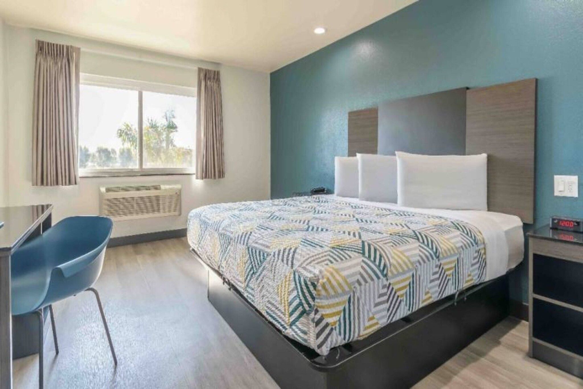 Een hotelkamer met een bed, bureau, stoel en een raam met gordijnen.