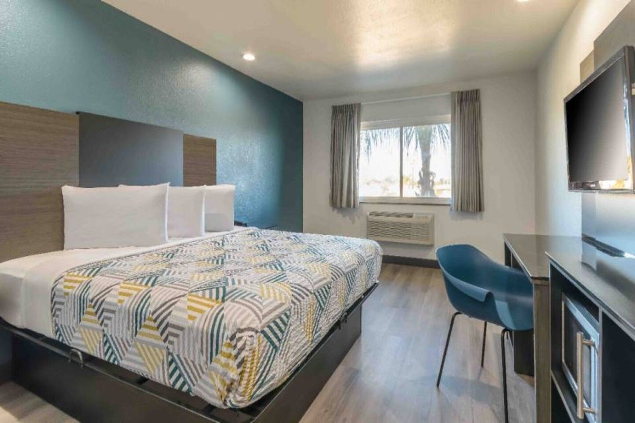A hotel room with a bed, a desk, a chair, a TV, and a window with curtains.