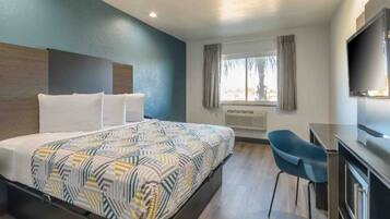 A hotel room with a bed, a desk, a chair, a TV, and a window with curtains.