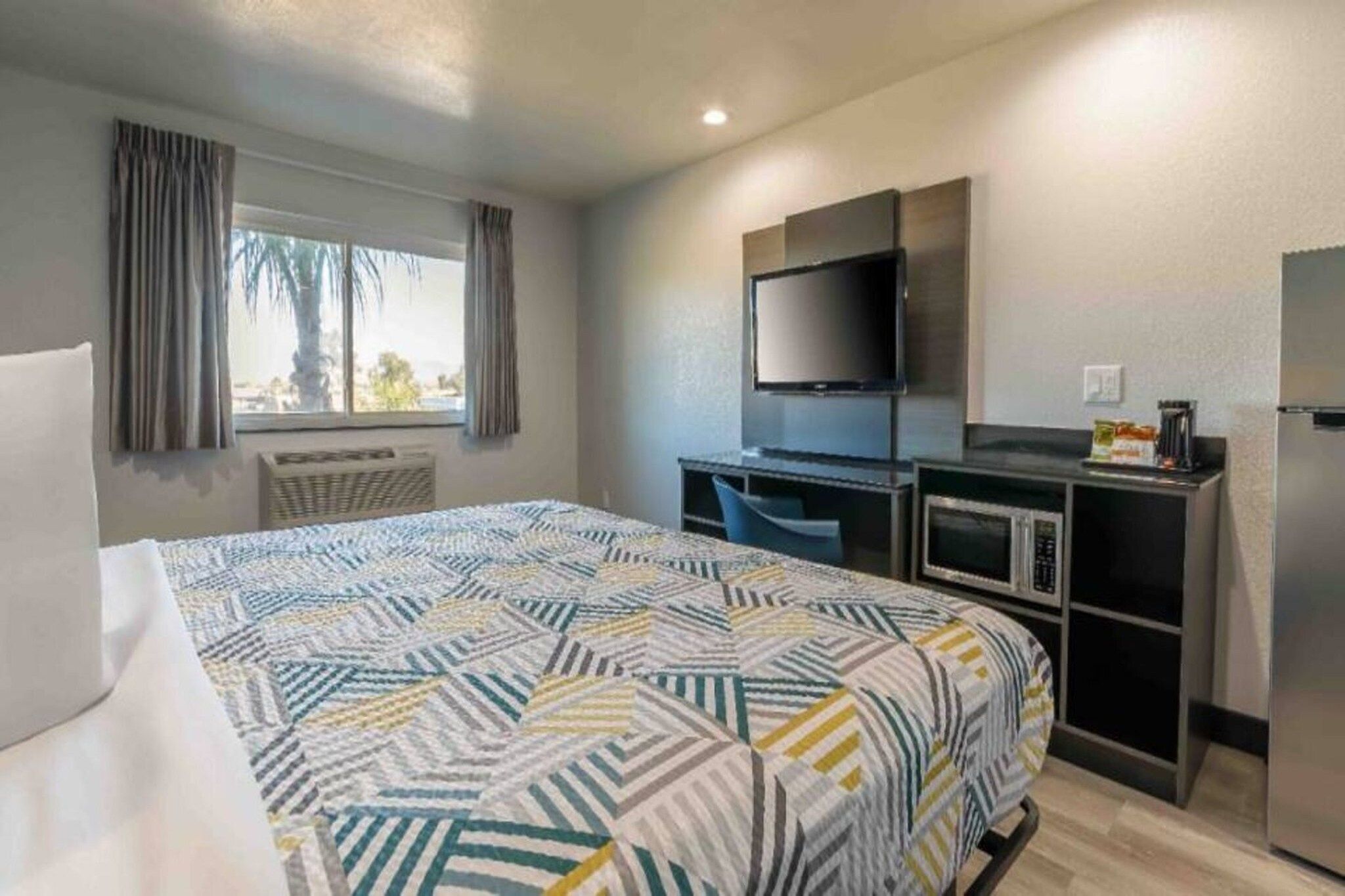 Ein Hotelzimmer mit einem Bett, einem Schreibtisch, einem Fernseher, einer Mikrowelle und einem Kühlschrank.
