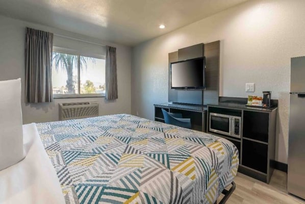 A hotel room with a bed, a desk with a television, a microwave, and a refrigerator.