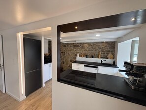A modern kitchen with a stone wall backsplash, a coffee machine, and a black countertop. - Just 5 meters from the sea—a charming Breton house. (Porspoder)