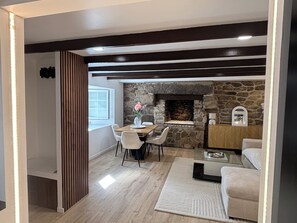 A modern living room with a stone fireplace, a dining area with a table and chairs, and a cozy seating area with a sofa and a side table. - Just 5 meters from the sea—a charming Breton house. (Porspoder)