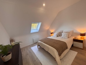 A bedroom with a sloped ceiling, a skylight, a bed with white bedding, two bedside tables with lamps, and a potted plant. - Just 5 meters from the sea—a charming Breton house. (Porspoder)
