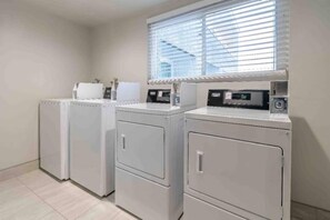 A laundry area with three stacked washing machines and dryers, a window with blinds, and a tiled floor.